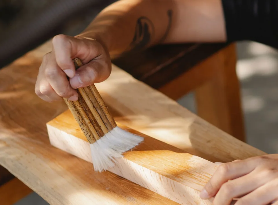 Craftsman applying a clear wood finish with a brush in a workshop.